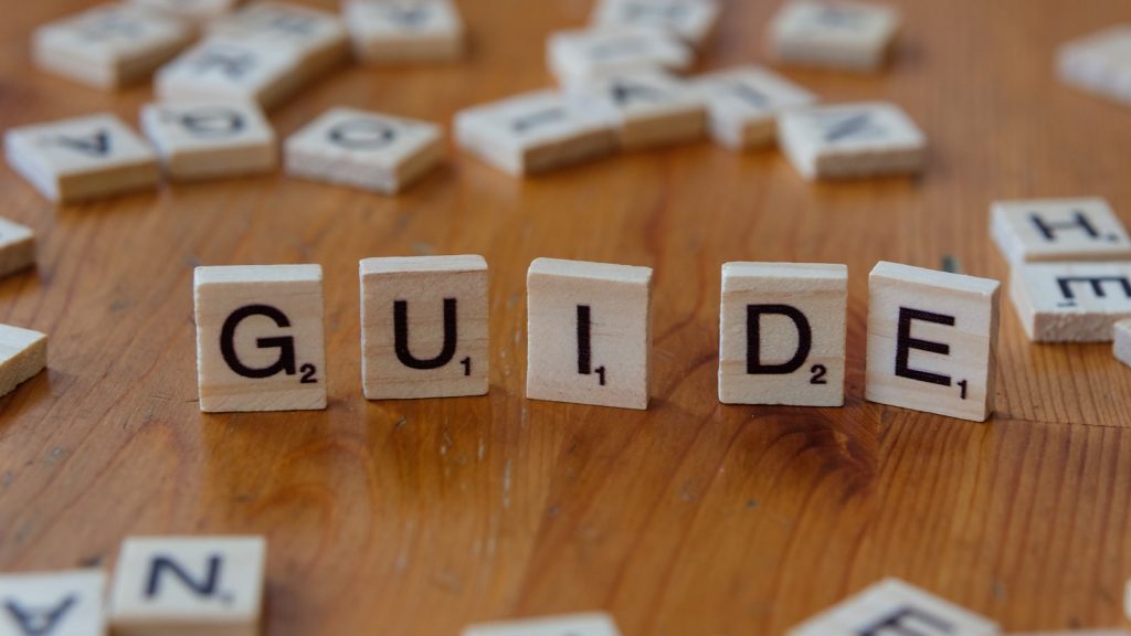 A wooden table topped with scrabble tiles spelling the word guide